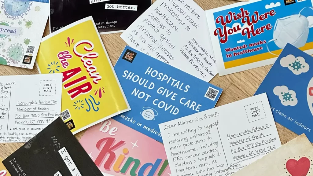 A scattering of colourful printed postcards from DoNoHarm BC include slogans like Clean the Air, Hospitals should give care not Covid, and Be Kind (protect the vulnerable). Between them, postcard backs have hand-written messages to Health Minister Adrian Dix.