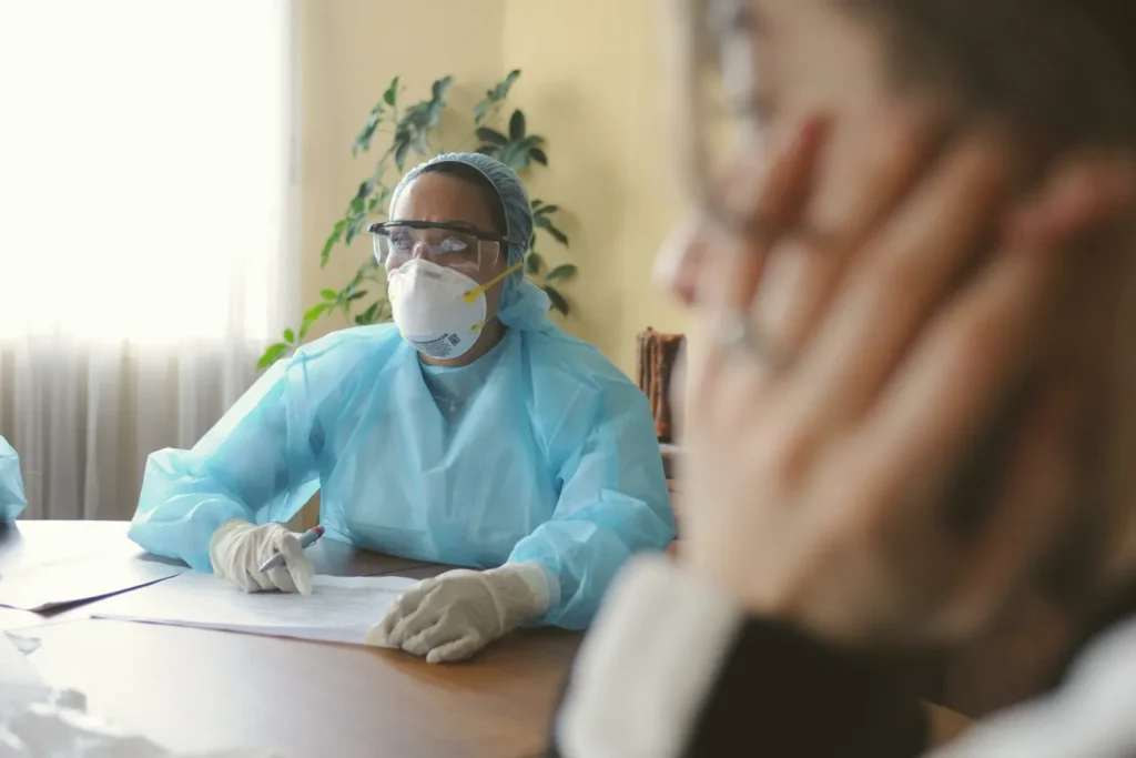 Pushing for a national N95 masking standard news article. Image shows a healthcare worker at a meeting table wearing an N95 mask and disposable gown, gloves and hair net.